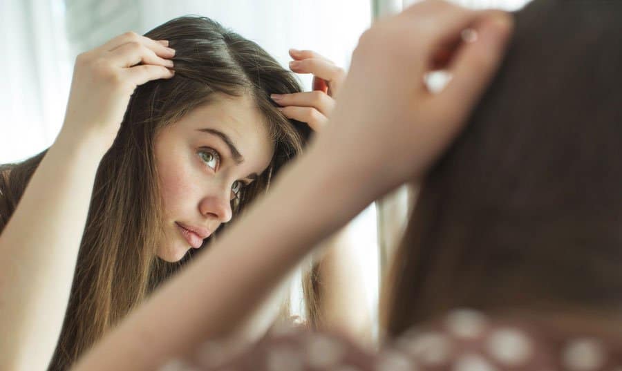 Woman with long straight hair checking to see if her hair is thinning.