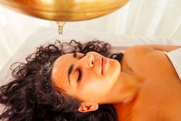Curly haired woman receiving an ayurvedic oil treatment or oil rinse for her hair.
