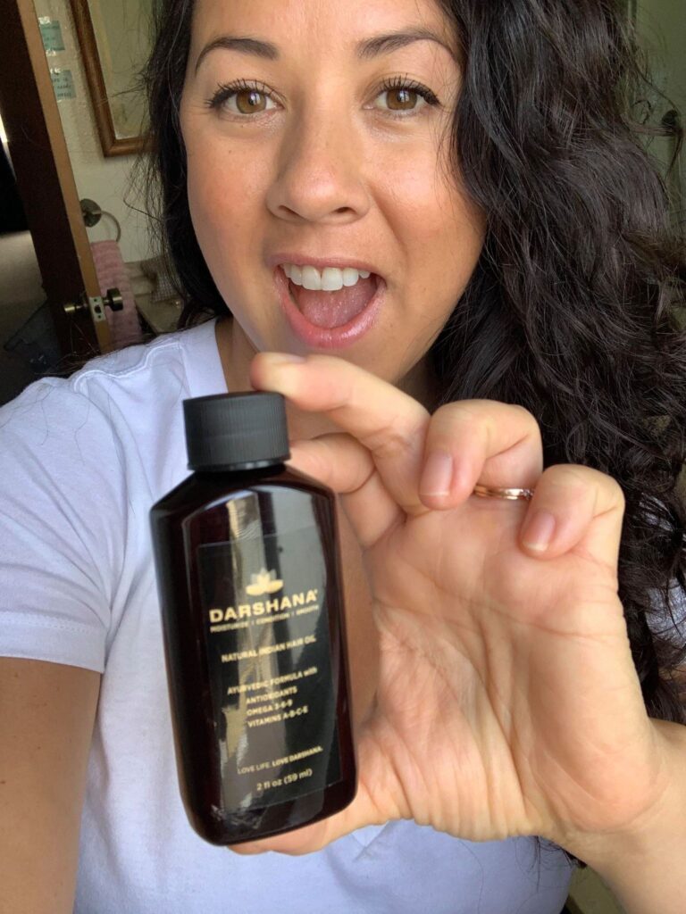 Smiling brunette woman holding Darshana Indian hair oil