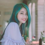 Beautiful young woman with vibrant green hair smiling happily indoors.